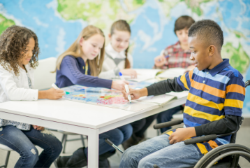 5 students sitting around a desk marking a world map, one student in wheelchair