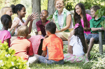 teacher and students sitting outside in a circle smiling